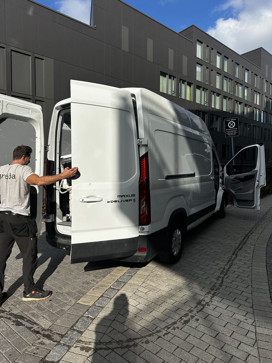 Greida-montør ved en elektrisk varebil med åpne bakdører i en bygate