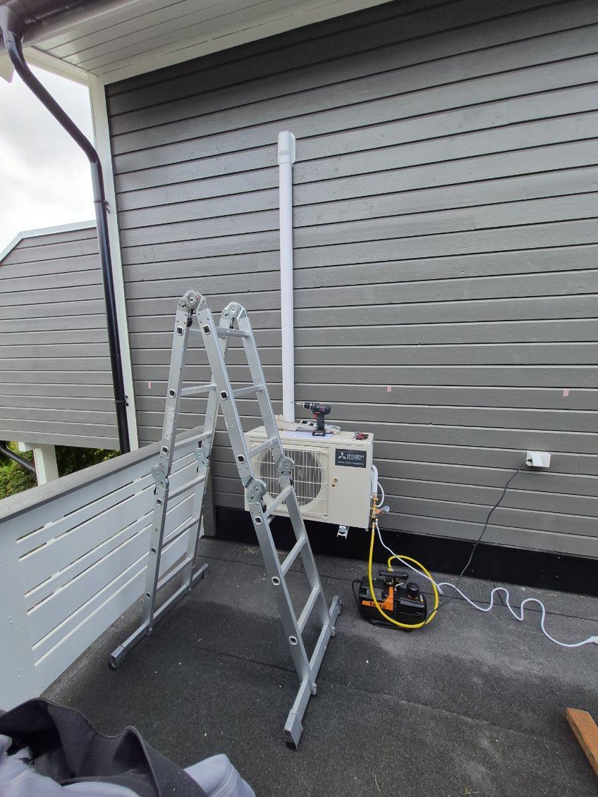 Utedel til varmepumpe montert på en terrasse, med stige og verktøy